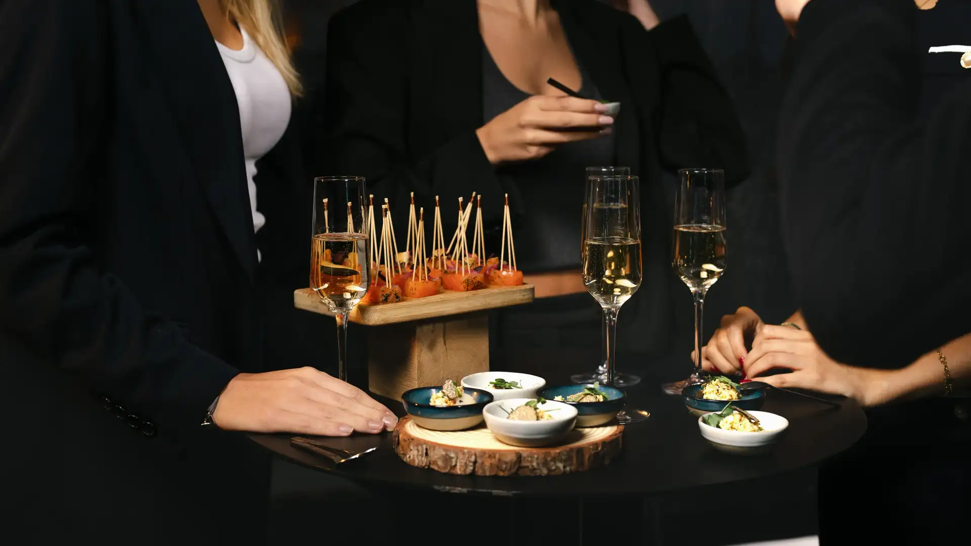 Several people in formal attire around a table with glasses of champagne and plates of appetizers.