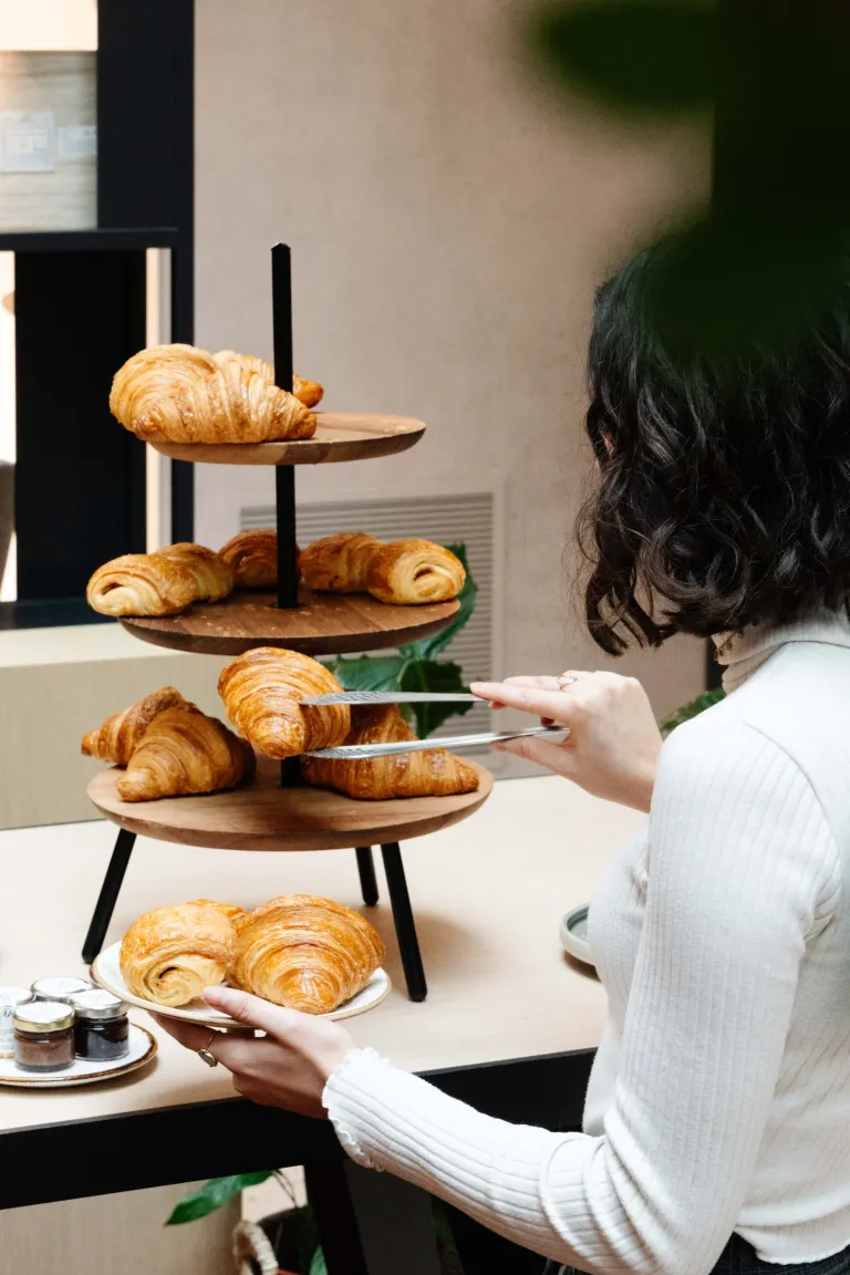 Une personne prend un croissant sur un présentoir à trois étages rempli de viennoiseries