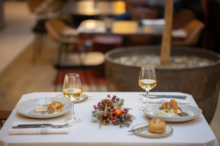 Table dressée avec deux assiettes de nourriture, deux verres de vin blanc, des couverts et une décoration de centre de table composée de branches et de baies